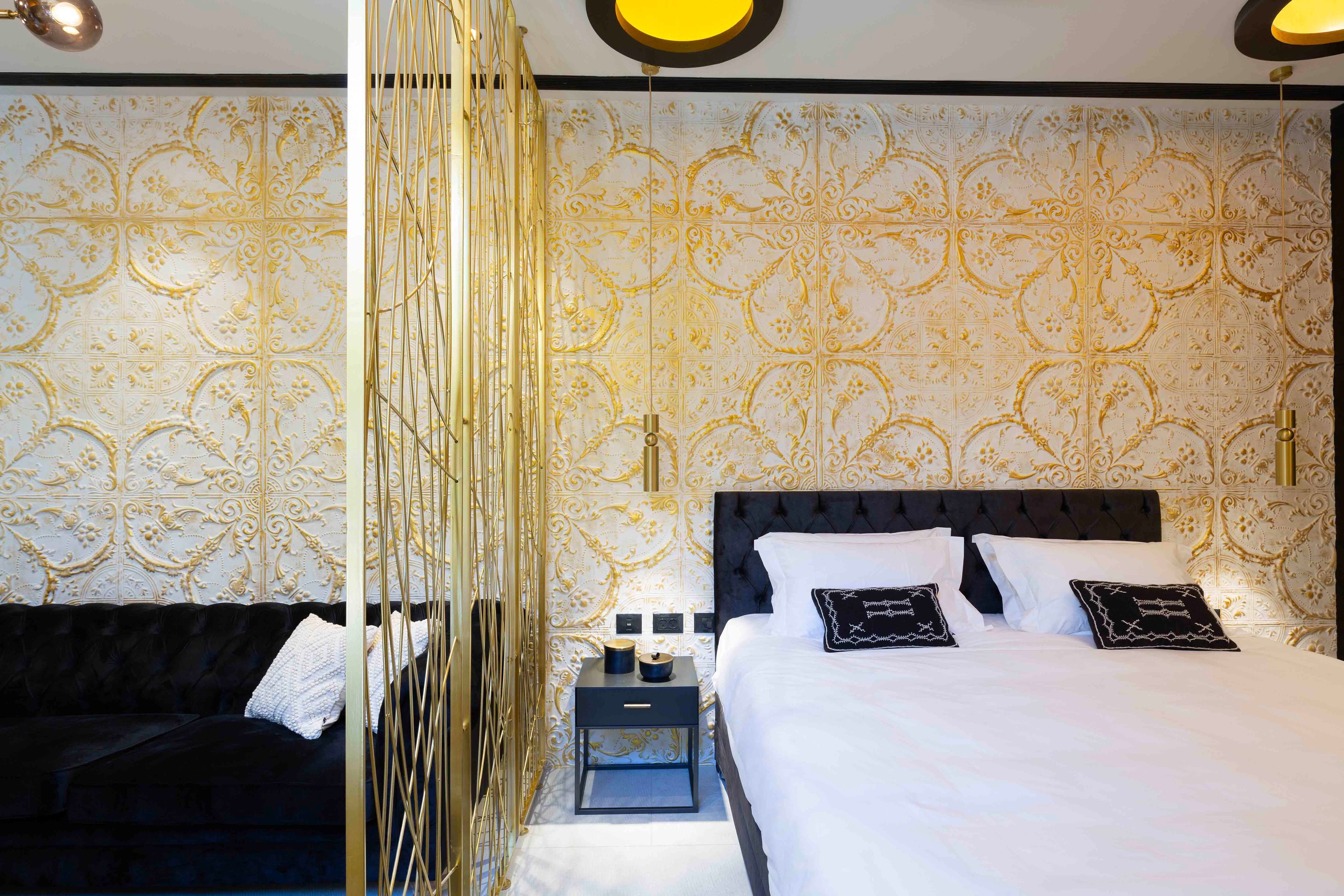 Une chambre d’hôtel avec un grand lit, un canapé de couleur sombre et un mur décoratif orné de motifs complexes.