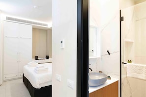 A modern hotel room with a bed, a bathroom with a large mirror, and a white wardrobe. - The Shell House (Tel Aviv)