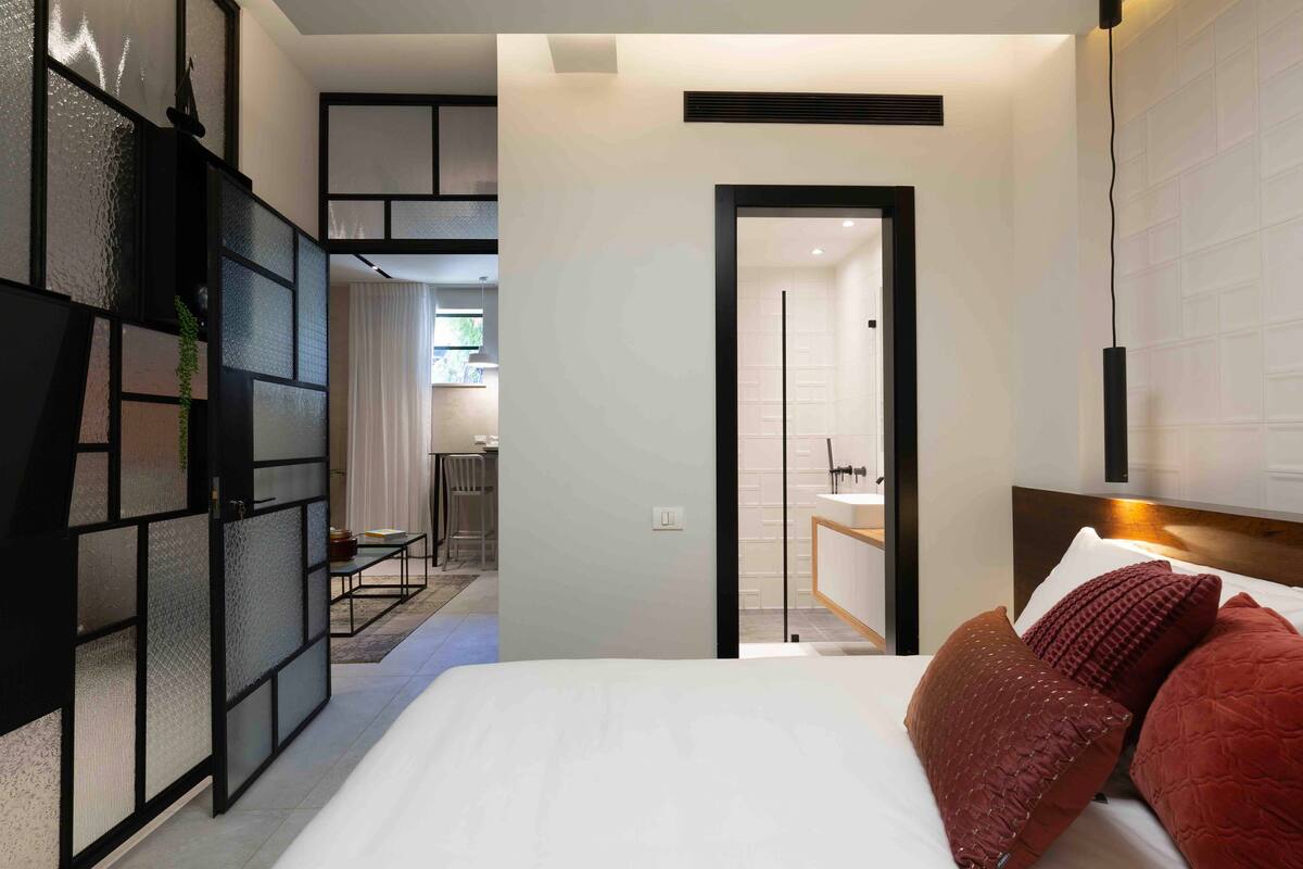 A modern hotel room with a large bed, a desk, and a view into the dining area.