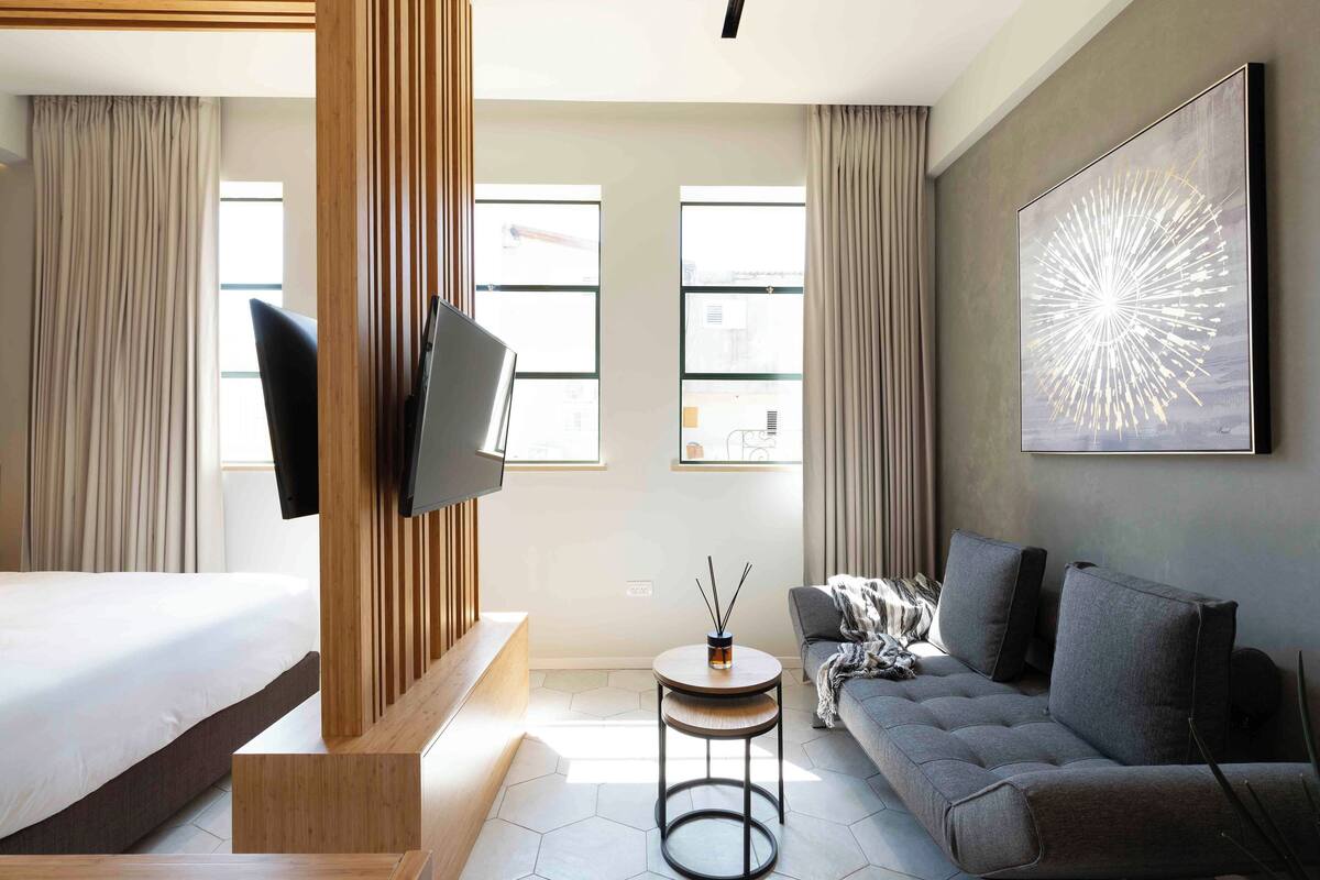 A modern hotel room with a bed, sofa, TV, and artwork.