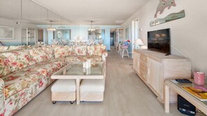 Uma sala de estar moderna com um sofá floral, uma mesa de centro de vidro e um armário de madeira com uma TV.