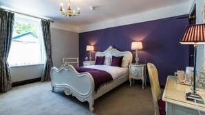 A bedroom with a white ornate bed, two bedside tables with lamps, a chair, and a desk with a lamp.