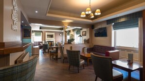 A spacious lobby with a wooden reception desk, comfortable seating areas, and a large window providing natural light.