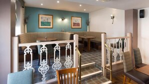 A restaurant with a cozy seating area, a staircase with ornate railings, and framed artwork on the walls.