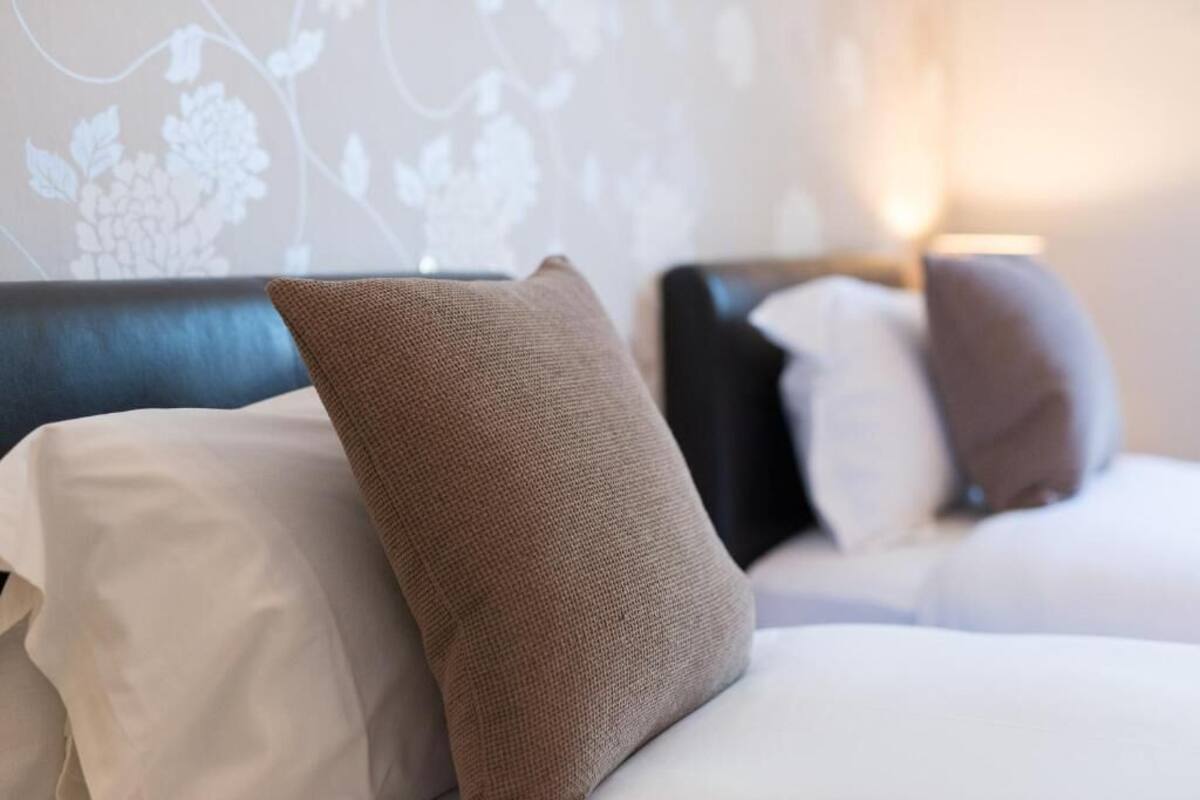 A hotel room with a neatly made bed, a headboard, and a floral wallpaper pattern.