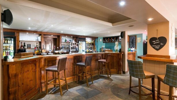 A bar area with wooden bar counters, stools, and a variety of bottles.