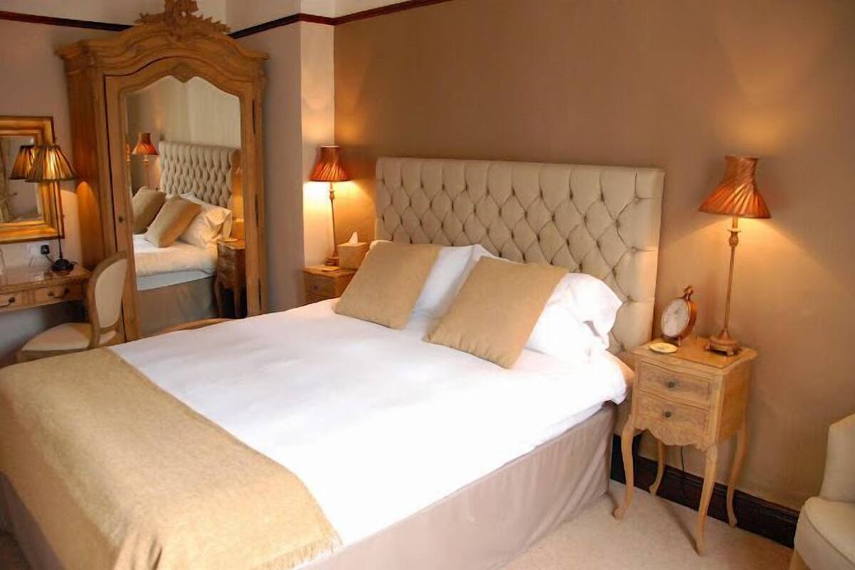 A neatly made bed with a tufted headboard, bedside tables with lamps, and a mirror on the wall.