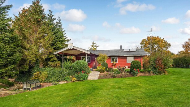 A red house with a covered porch, surrounded by a well-maintained lawn and various plants.