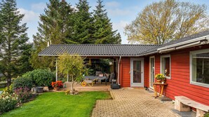 A red house with a tiled roof, a covered porch, and a brick pathway leading to the entrance.