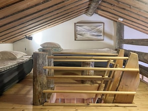 Ein Schlafzimmer im Loft-Stil mit schrägverdeckter Decke, einem hölzernen Bettgestell, einem Etagenbett und einem gerahmten Landschaftsbild an der Wand.