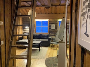 Ein rustikales Blockhaus-Interieur mit Schlafgalerie, einer Couch, einem Esstisch und einem großen Fenster.