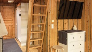 Un intérieur en bois avec une commode blanche, un petit tabouret, une échelle et un téléviseur fixé au mur.