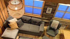 L’intérieur d’un chalet confortable, avec un canapé gris, une petite table ronde et un fauteuil vert.