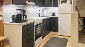 Une cuisine compacte avec des meubles noirs, un plan de travail blanc, une machine à café, une bouilloire et un four à micro-ondes.
