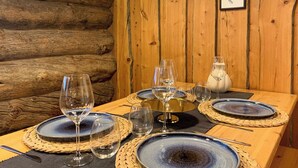 Une table de salle à manger en bois, mise avec des assiettes bleues, des verres à vin transparents et un vase blanc.