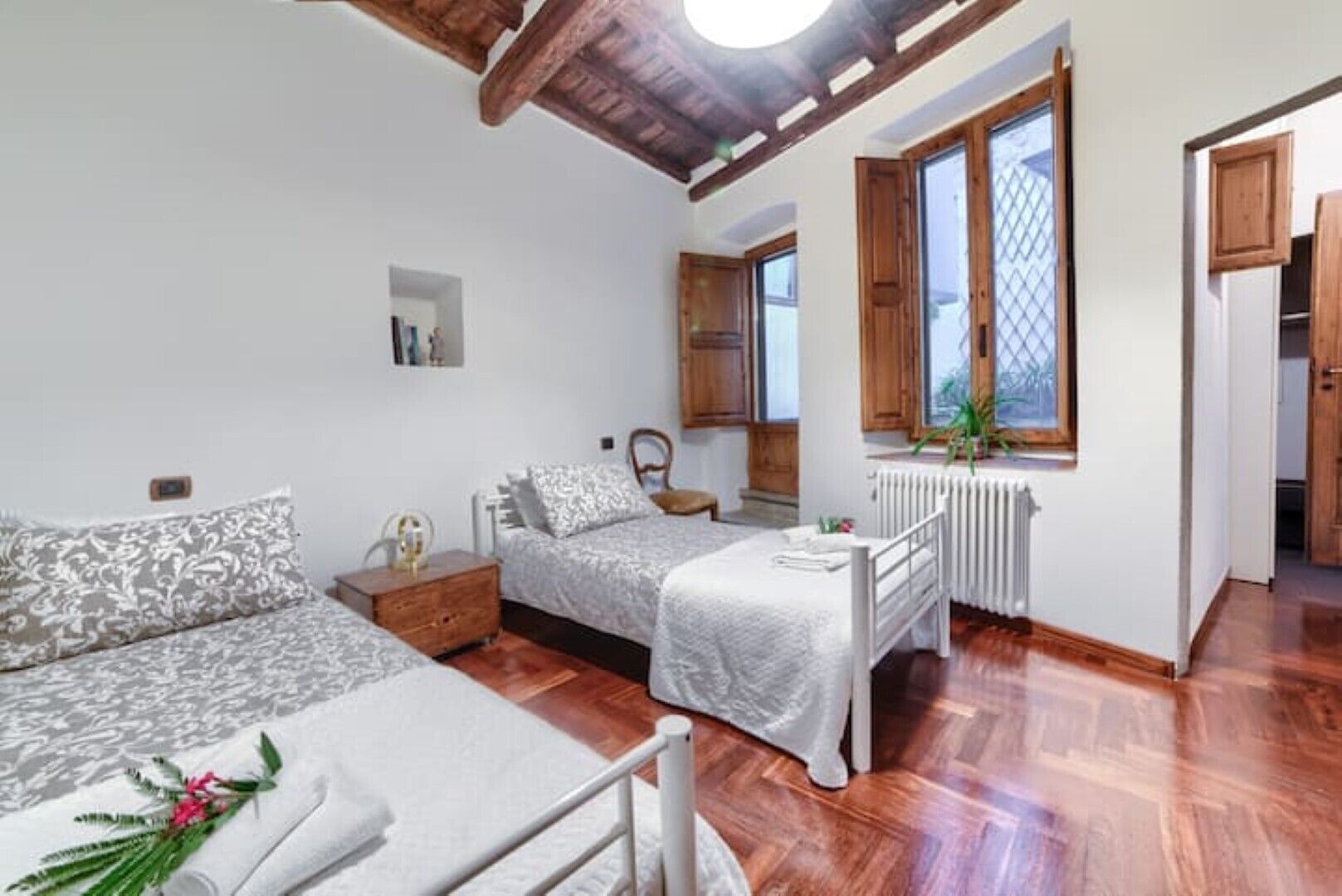 A bedroom with two beds, wooden flooring, a radiator, and a window with wooden shutters.