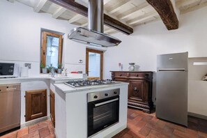 Una cocina con estufa a gas, horno, refrigerador de acero inoxidable, armarios de madera y una ventana con marco de madera.