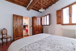 Un dormitorio con una cama grande, un armario de madera y una silla. Hay una ventana y un radiador.