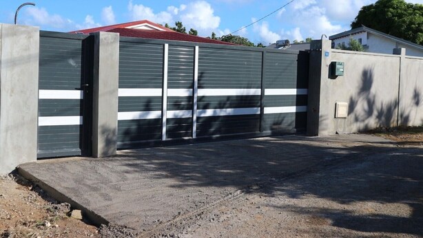 A gated parking area with a concrete wall and a metal gate. - House well located in La Jaille in the center of Guadeloupe (Baie-Mahault)