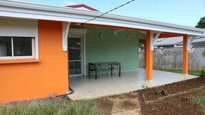 A house with an orange exterior, a covered patio with a table and chairs, and a visible window. - House well located in La Jaille in the center of Guadeloupe (Baie-Mahault)