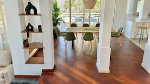 Een moderne woonkamer met een eethoek, houten vloeren en een groot raam met uitzicht op de natuur.