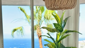 Een eettafel met een groene placemat, een geweven hanglamp en uitzicht op de oceaan door grote ramen.