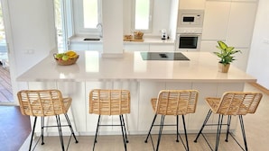 Een moderne keuken met een centraal eiland, vier rieten barstoelen, een magnetron, een oven en een potplant.