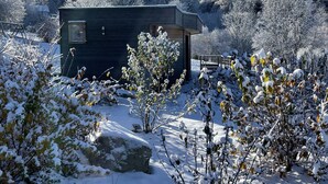 A small cabin with a dark exterior, surrounded by snow-covered ground and trees. - Nature Cottage Vosges Le Renard (Anould)