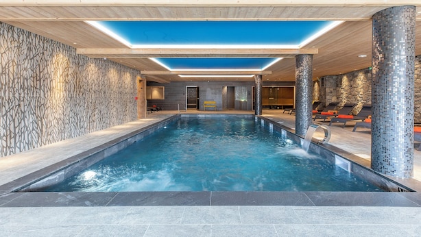 Une piscine intérieure au design moderne, dotée d’une verrière et de murs en mosaïque.
