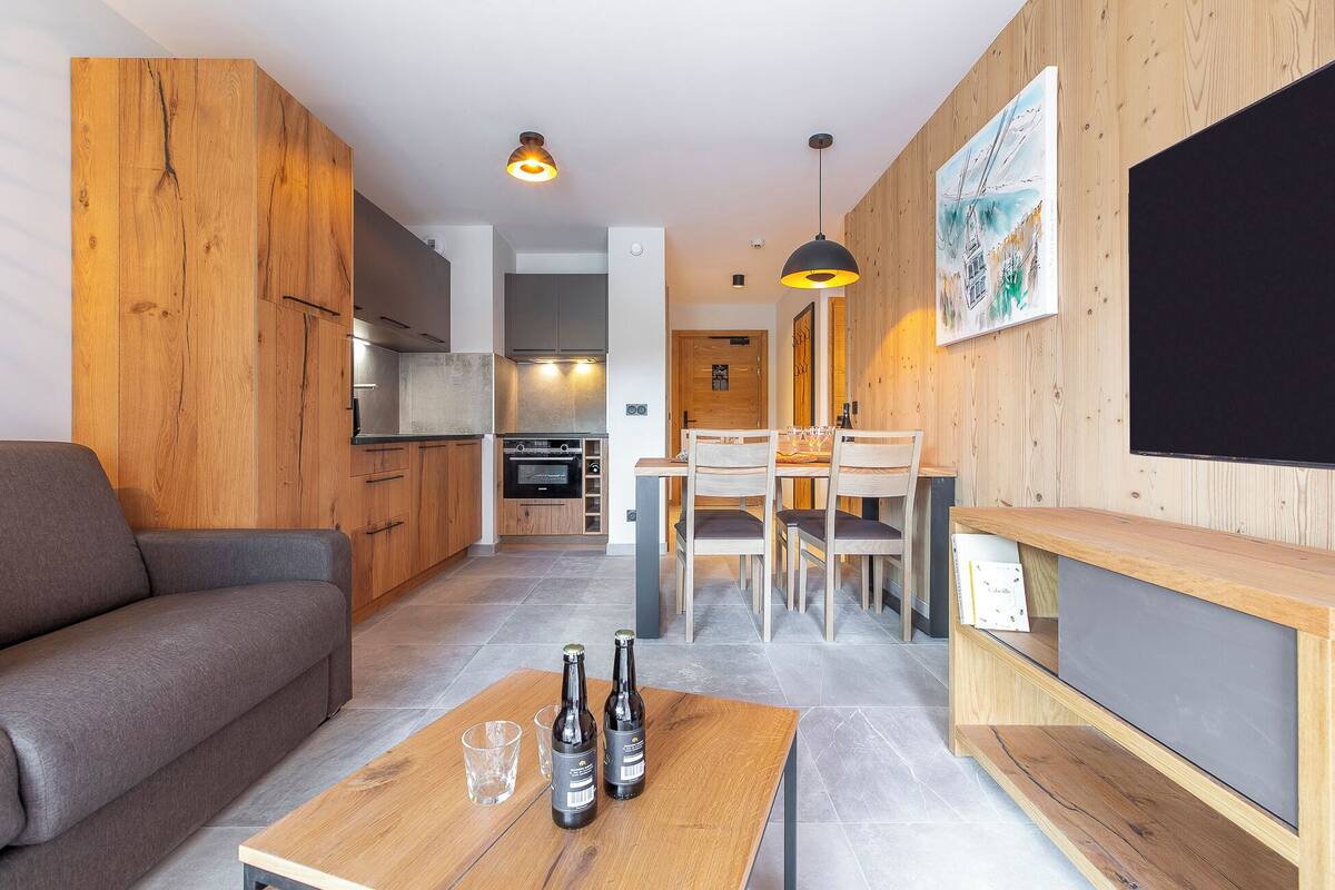 Une cuisine moderne avec des meubles en bois, un coin repas avec une table et des chaises, et un salon avec un canapé.