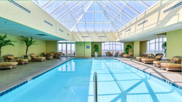An indoor swimming pool with lounge chairs and potted plants, surrounded by large windows.
