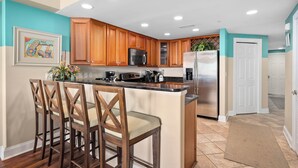 A kitchen with wooden cabinets, a central island with bar stools, stainless steel appliances, and recessed ceiling lights.
