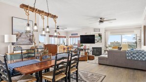 A spacious living room with a wooden dining table, dark chairs, and a gray sofa. A flat-screen TV is mounted on the wall, and a ceiling fan is visible. - ** Prices dropped $300 per week, for all remaining 2023 weeks. Prices shown include the discount. **<br>Avalon Penthouse 803 - 1 of a kind 3 br/3 bath with huge balcony and incredible views. (Ocean City)
