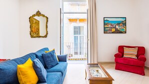 Una sala de estar con un sofá azul, un sillón rojo, una mesa de centro de madera, un espejo con marco dorado y un cuadro en la pared.