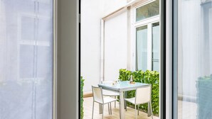 Un balcón con una mesa y sillas de vidrio, una planta en maceta y vistas a la calle.