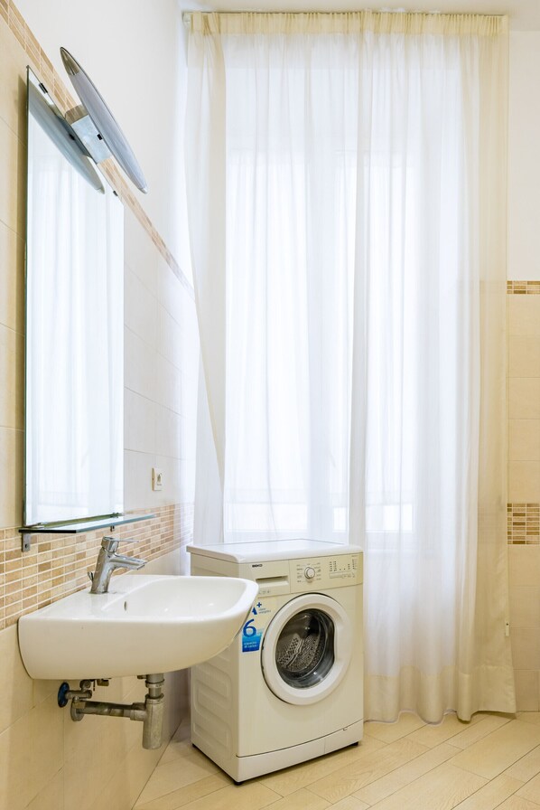 Een badkamer met een witte wastafel, een wasmachine en een douchegordijn.
