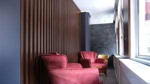 Een moderne kamer met een wand van houten latten, een rode bank, een gele stoel en een groot raam met uitzicht op de stad.