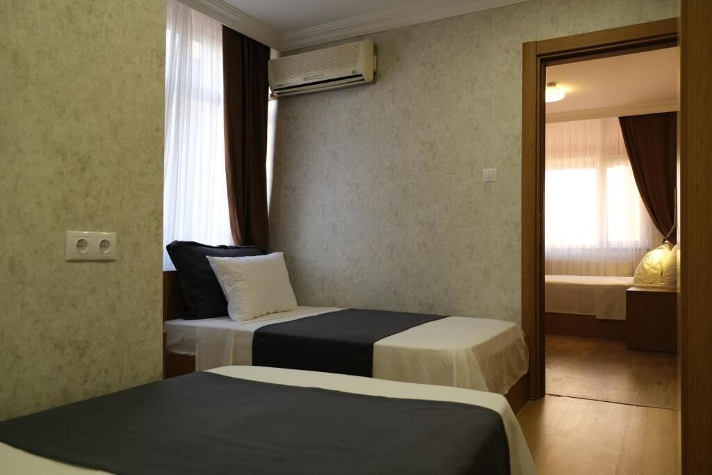 A hotel room with two beds, a window with curtains, an air conditioning unit, and a door leading to another room.