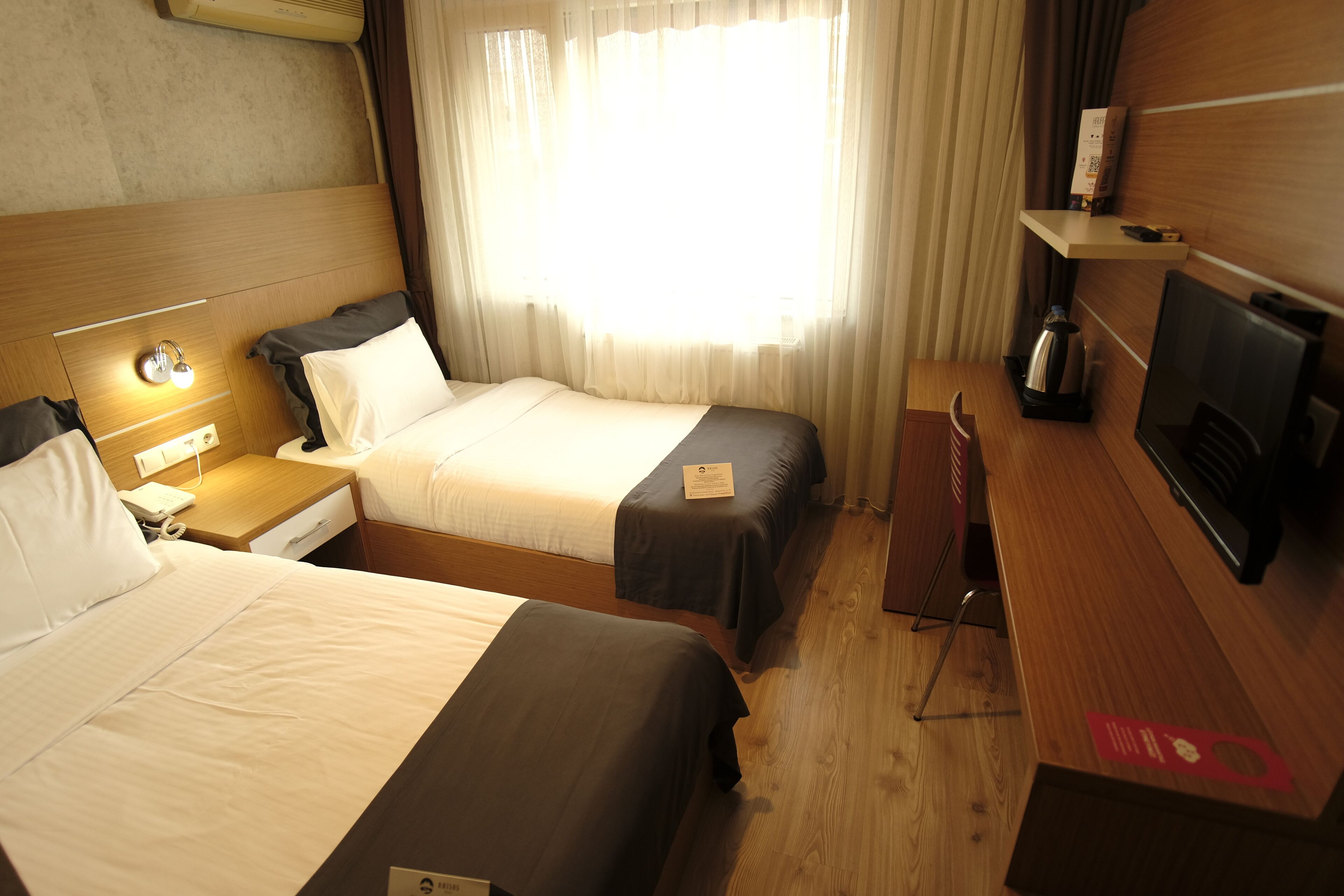 Une chambre d’hôtel avec deux lits, un bureau en bois, une télévision et une fenêtre avec des rideaux.