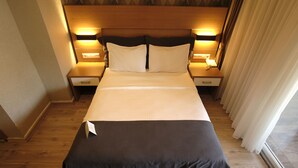 Een hotelkamer met een groot bed, een houten hoofdeinde, bedlampjes en een raam met gordijnen.
