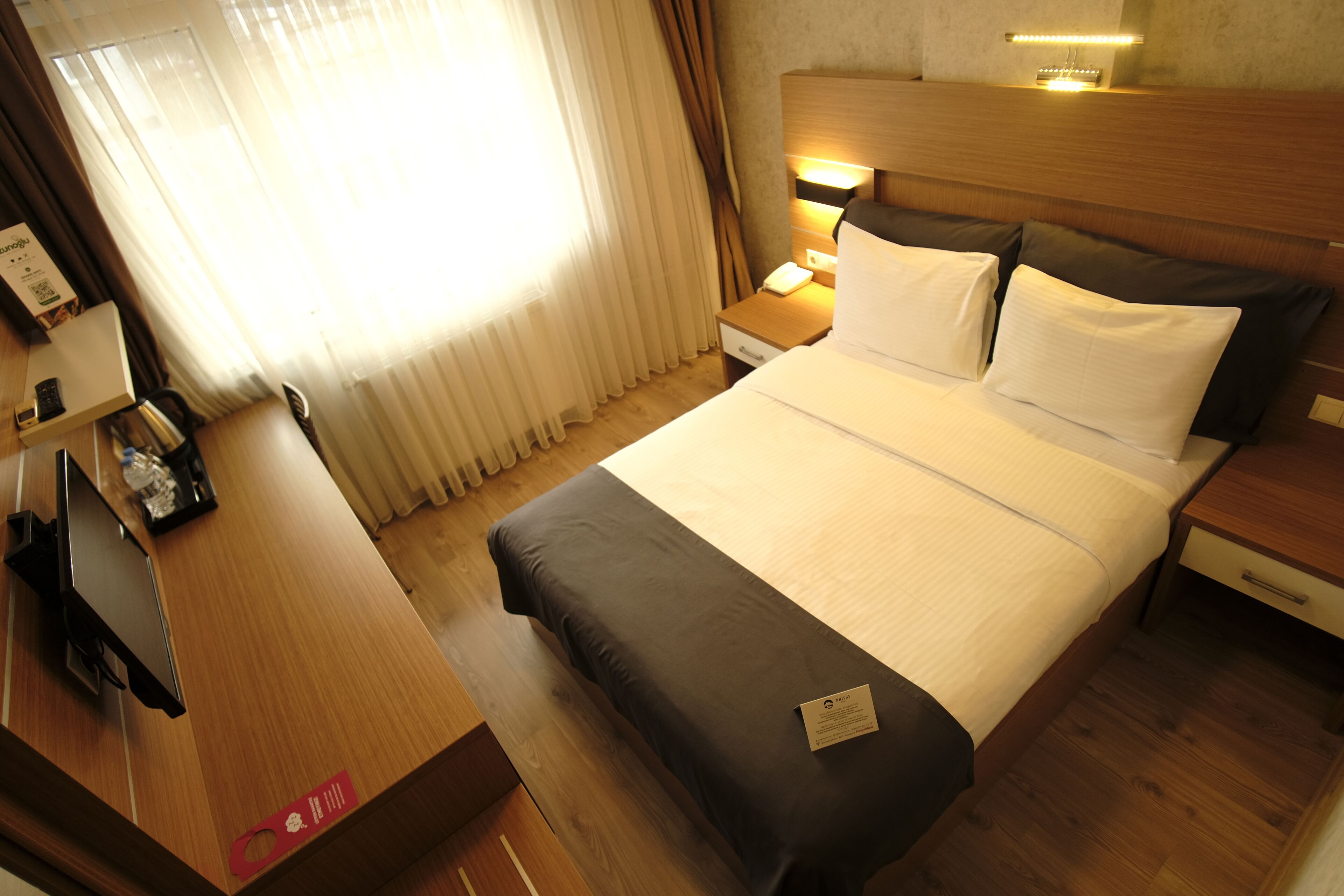 Habitación de hotel con cama, mesitas de noche, escritorio y ventana con cortinas.