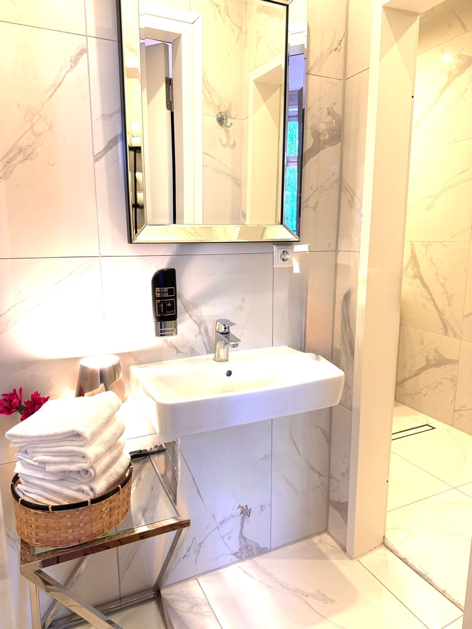A bathroom with a white sink, a mirror, a hand wash station, and a glass shelf with towels.