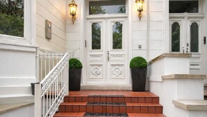 A set of red-tiled steps leading to a white door with two glass panels, flanked by two wall-mounted light fixtures. - Sleephotels Alsterroom (Hamburg)