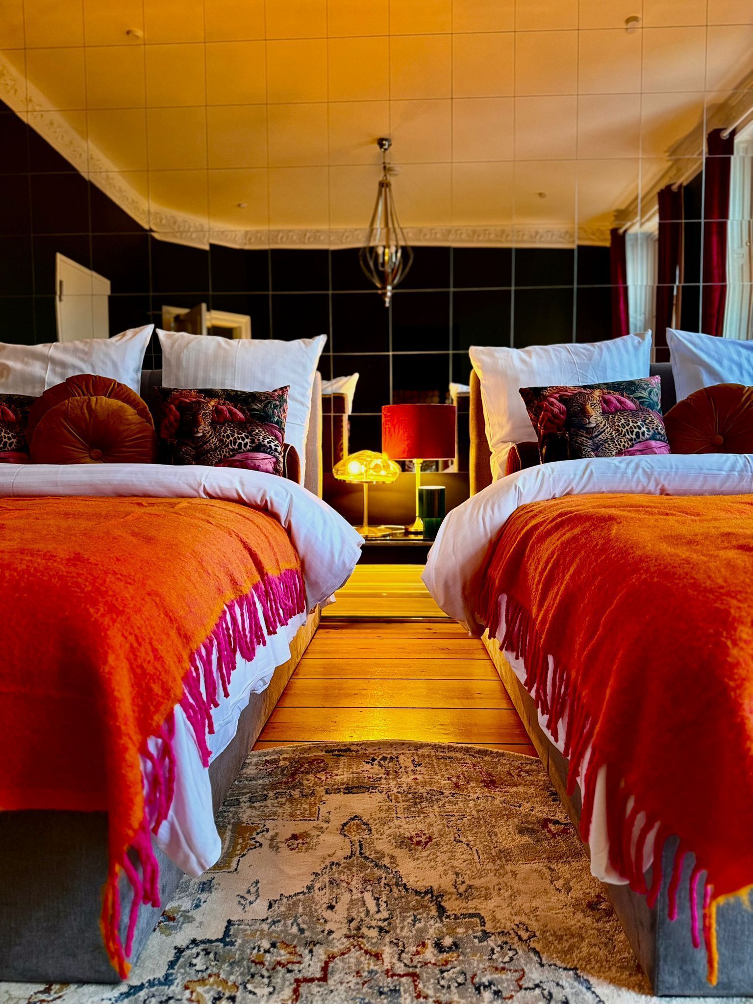 A hotel room with two beds, a patterned rug, and a chandelier.