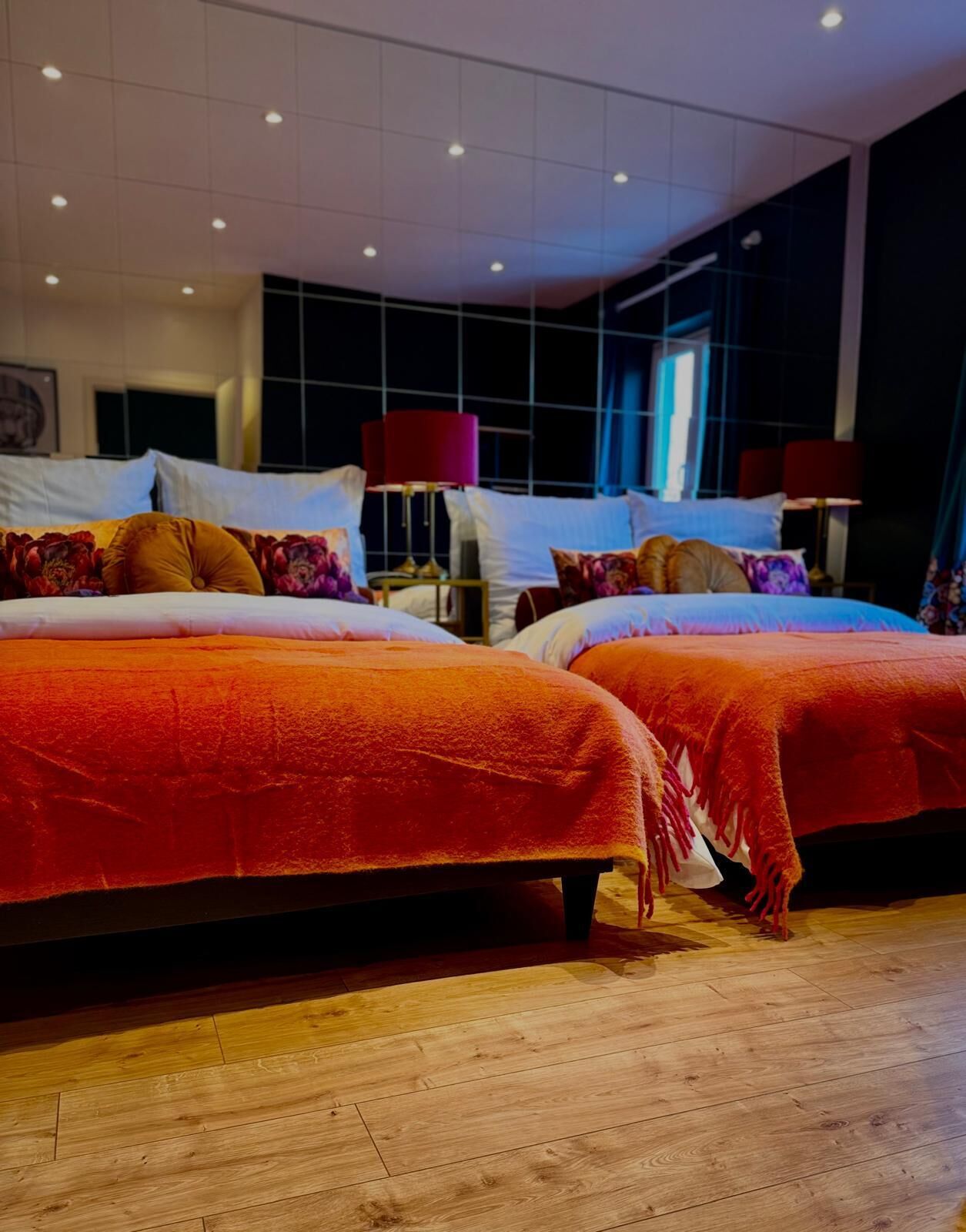 Quarto de hotel moderno com duas camas, soalho de madeira e uma grande janela com cortinas.