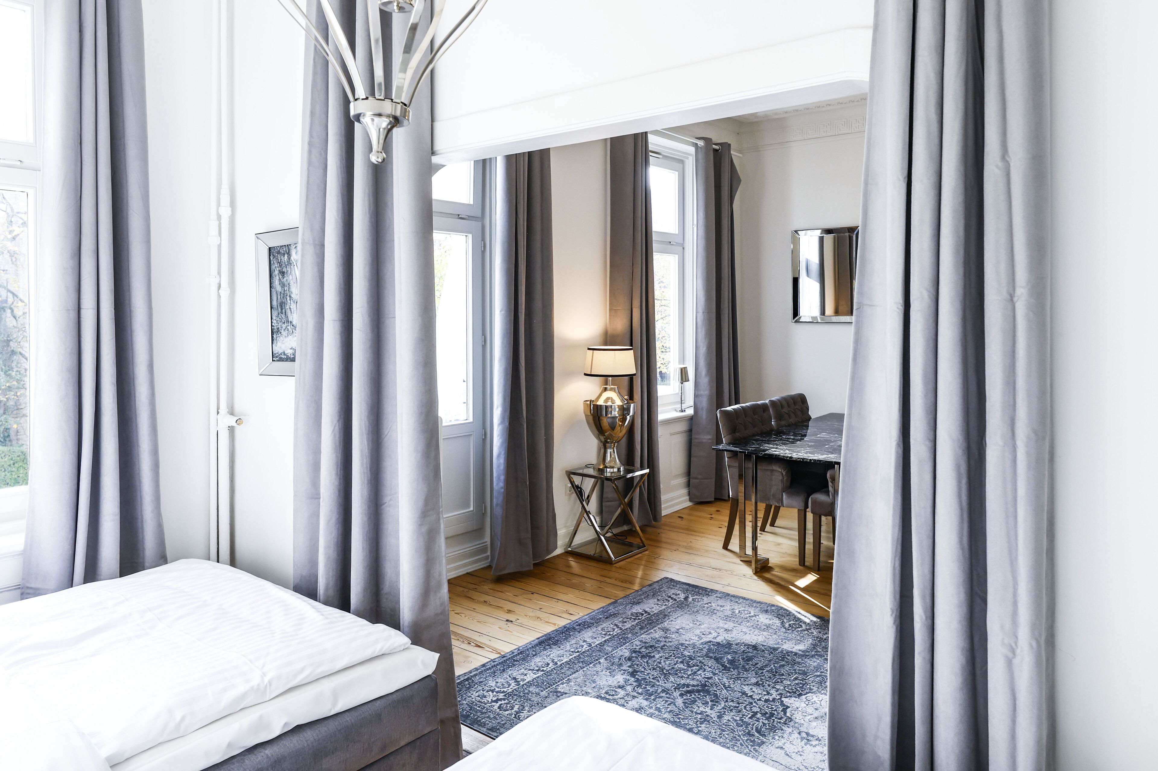 A bedroom with a bed, a desk, and a chair, with curtains and a lamp.