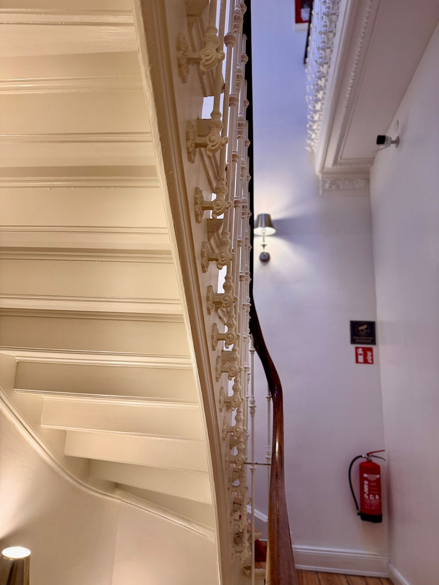 Een trap met versierde balustrades en een brandblusser aan de muur.