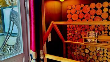A cozy room with a wooden bunk bed, a window with a decorative curtain, and a wall adorned with stacked logs.