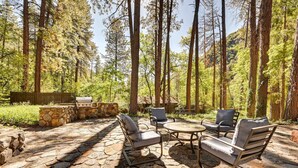An outdoor patio with stone flooring, surrounded by tall trees and a stone fireplace. - Patio & Mtn Views: Peaceful Sedona Retreat (Sedona)