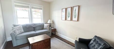 A living room with a grey sofa, a wooden coffee table, a black armchair, and a patterned rug.